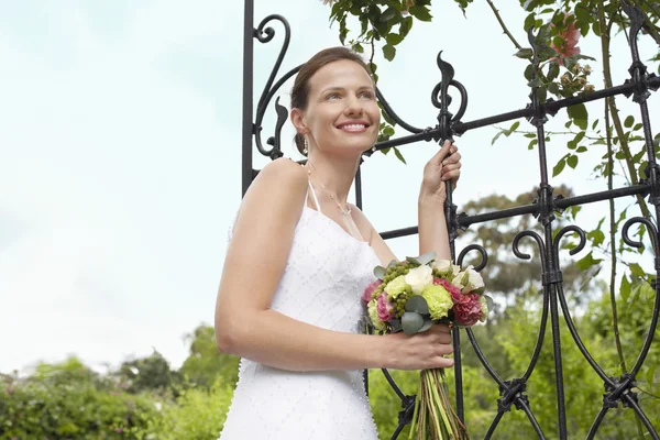 Bruid met boeket staande door poort — Stockfoto