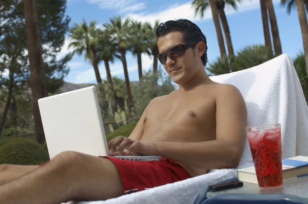 Homem sentado na cadeira de praia usando laptop — Fotografia de Stock