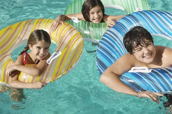 Rodzeństwo z nadmuchiwane Pontony, ciesząc się razem w basenie — Zdjęcie stockowe