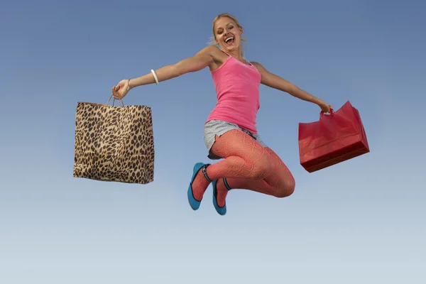 Vrouw springen met zakken tegen blauwe hemel — Stockfoto