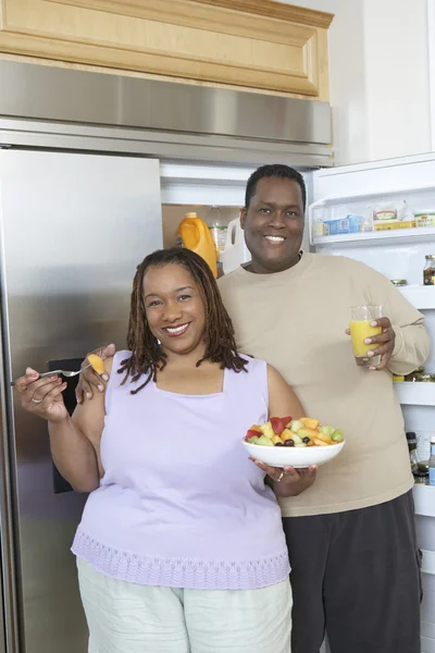 Casal com comida e bebida pelo refrigerador aberto — Fotografia de Stock