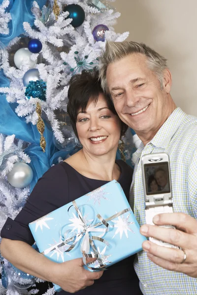 Pareja tomando autorretrato con teléfono celular delante del árbol de Navidad — Foto de Stock