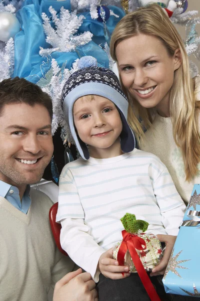 Pareja con hijo sosteniendo presente en frente de árbol de Navidad — Foto de Stock