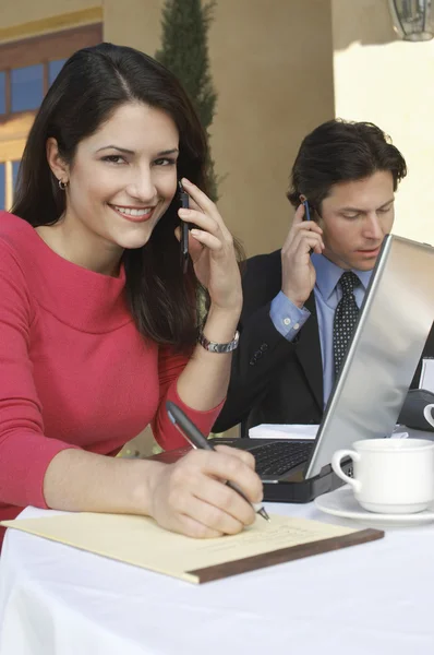 Geschäftsfrau schreibt, während sie mit dem Handy kommuniziert — Stockfoto