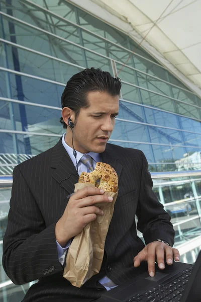 Geschäftsmann mit Laptop isst Bagel — Stockfoto