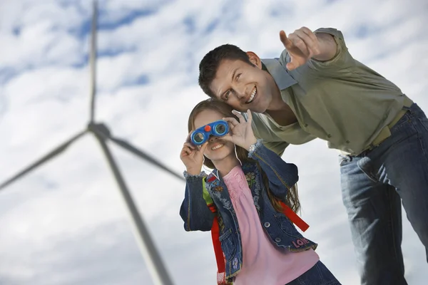 Chica usando prismáticos con padre en el parque eólico — Foto de Stock