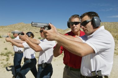 Instructor Assisting Officers With Hand Guns At Firing Range clipart