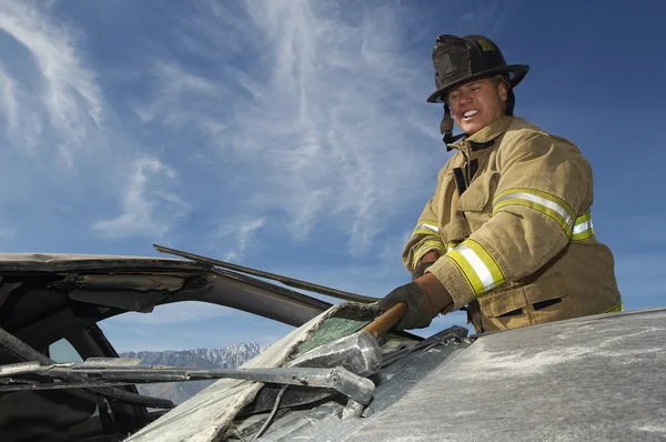 Tűzoltó üti a lezuhant autó kalapáccsal — Stock Fotó
