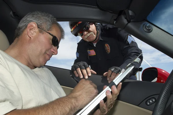 Polizist beobachtet Autofahrerin beim Unterschreiben von Papieren — Stockfoto