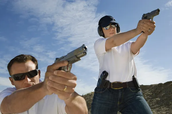 Homem e mulher apontando armas de mão em alcance de fogo — Fotografia de Stock