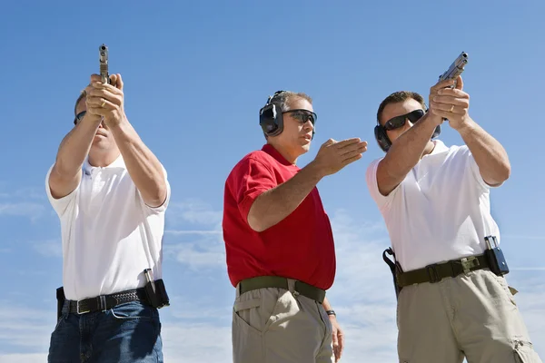 Instruktör hjälper män med hand kanoner på firing range — Stockfoto