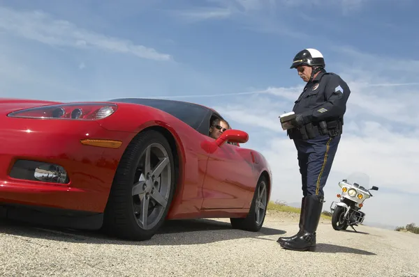 Дорожный полицейский разговаривает с водителем спортивного автомобиля Стоковая Картинка
