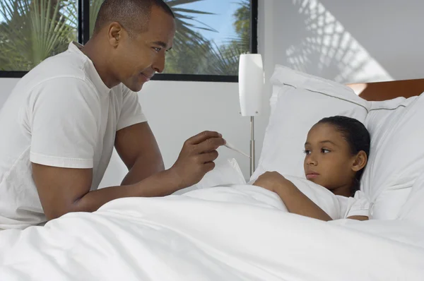 Pai verificando a temperatura da filha na cama — Fotografia de Stock