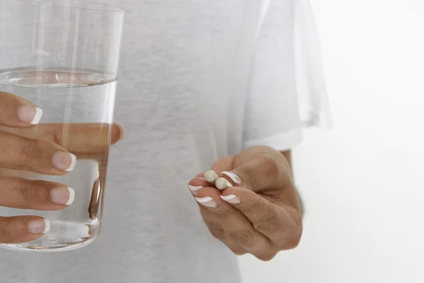 Mulher segurando pílulas e vidro de água — Fotografia de Stock