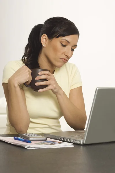 Mulher segurando xícara de café enquanto olha para o laptop — Fotografia de Stock