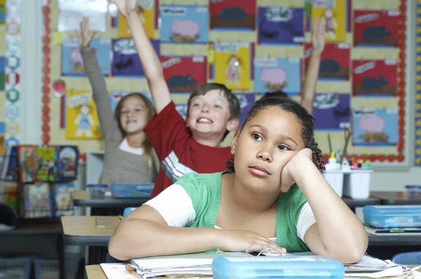 Uttråkad tjej med klasskamrater öka händer i bakgrunden — Stockfoto