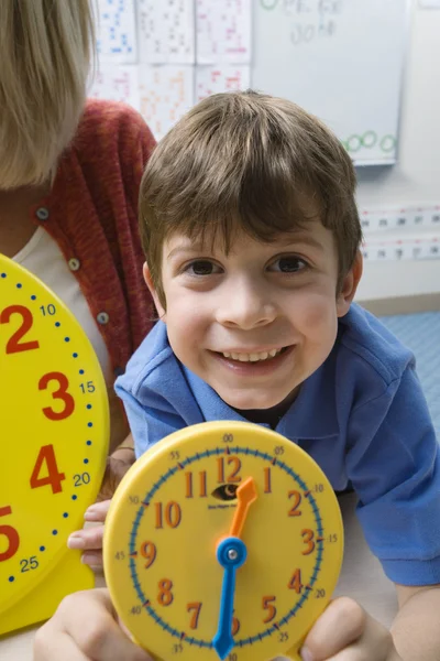 Junge zeigt gelbe Uhr mit Lehrer im Hintergrund — Stockfoto