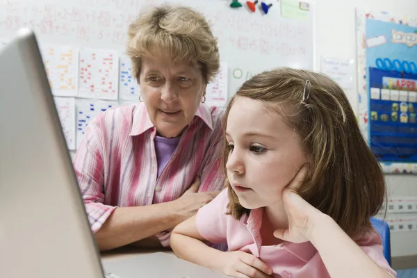 Nauczyciel pomaga uczennica użytkowania laptopa — Zdjęcie stockowe