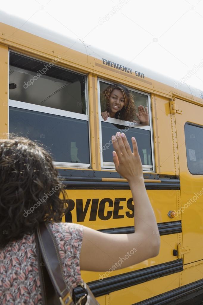 Mother waving to daughter on school bus