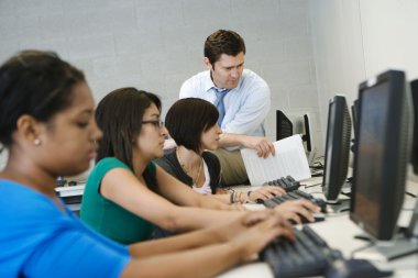 öğretmen bilgisayar laboratuarında öğrencilere yardım