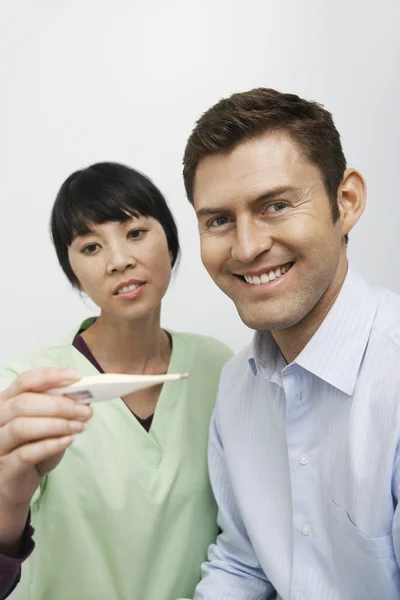 Счастливый пациент с женщиной-врачом смотрит на термометр — стоковое фото