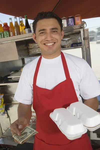 Jovem vendedor com dinheiro e comida — Fotografia de Stock