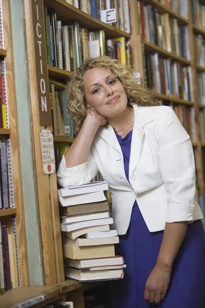 Vrouwelijke bibliothecaris permanent door stapel boeken — Stockfoto