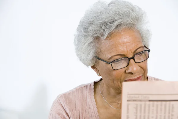 Mujer mayor leyendo acciones y acciones en el periódico — Foto de Stock