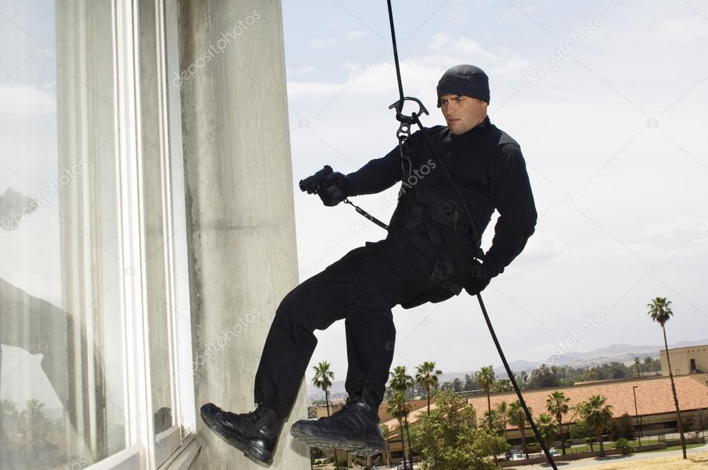 SWAT Team Officer Rappelling And Aiming Gun