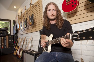 gitar store içinde oturan yetişkin adam orta ciddi portresi