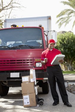 Young delivery man looking at delivery list on clipboard with truck in background clipart