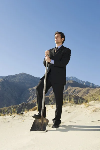 Бизнесмен держит лопату в пустыне — стоковое фото