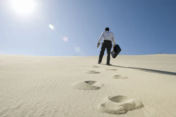 Бизнесмен, гуляющий с портфелем в пустыне — стоковое фото