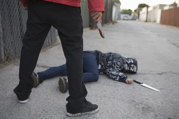 Мужчина стоит рядом с зарезанной женщиной, лежащей на земле — стоковое фото