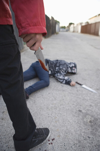 Преступник, стоящий рядом с зарезанным, лежащим на земле
