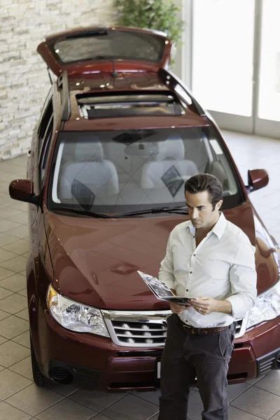 Μέσα ενήλικος άνθρωπος ανάγνωση έγγραφο μπροστά από το πολυτελές αυτοκίνητο σε εμφάνιση δωμάτιο — Φωτογραφία Αρχείου