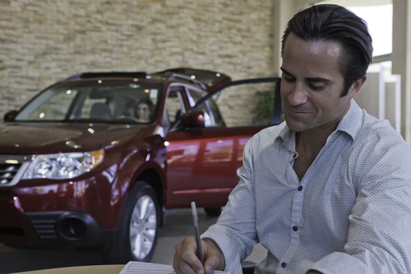 Hombre firmando papeles con coche en segundo plano —  Fotos de Stock