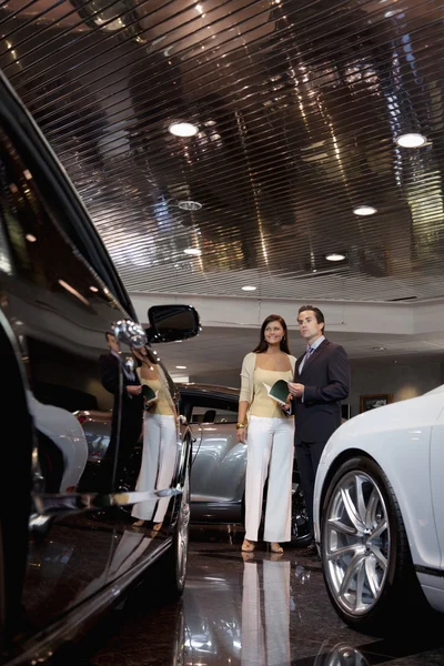 ショールームでの自動車のセールスマンと立っている女性 — ストック写真