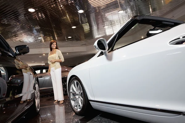 Toute la longueur de la femme souriante debout dans la salle d'exposition de voiture — Photo