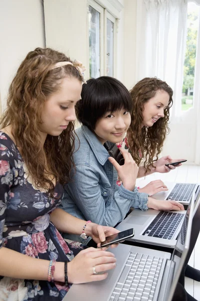 Três amigas usando laptop e celular — Fotografia de Stock