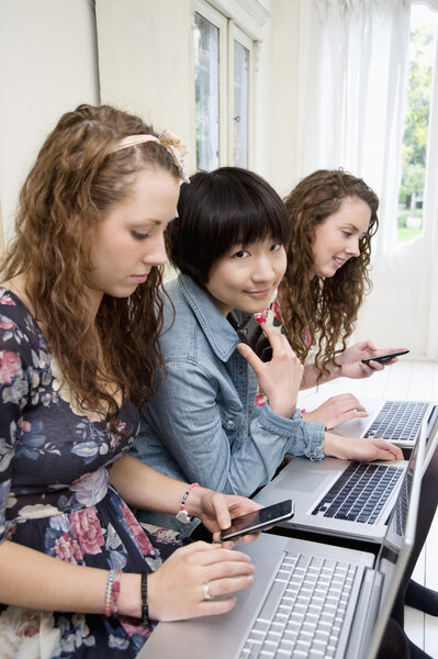 Three female friends using laptop and cell phone