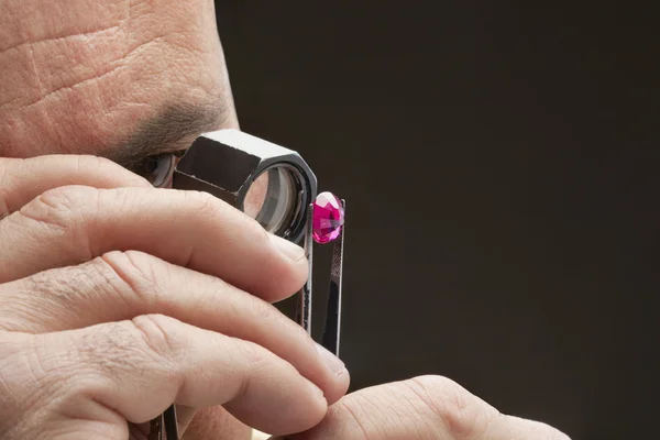 Cropped image of jeweler examining jewel over black background — Stock Photo, Image