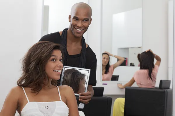 Hairdresser holding a mirror behind young woman — Stock Photo, Image