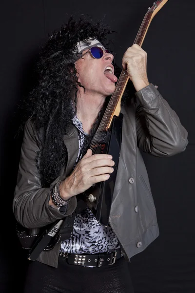 Senior man licking his guitar while performing over black background — Stock Photo, Image