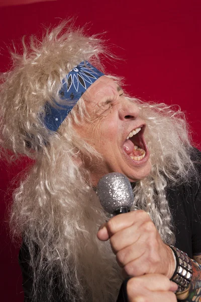 Close-up of senior male singer singing over red colored background — Stock Photo, Image