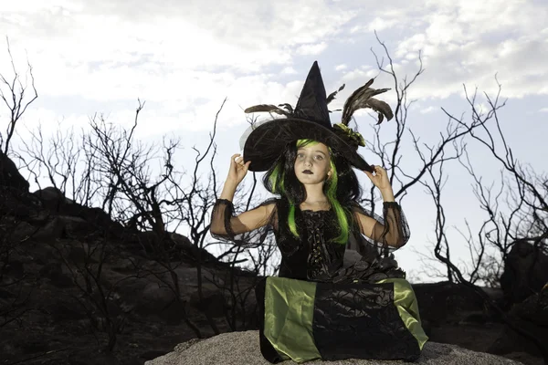 Menina sentada na pedra de rocha segurando seu chapéu de bruxa — Fotografia de Stock