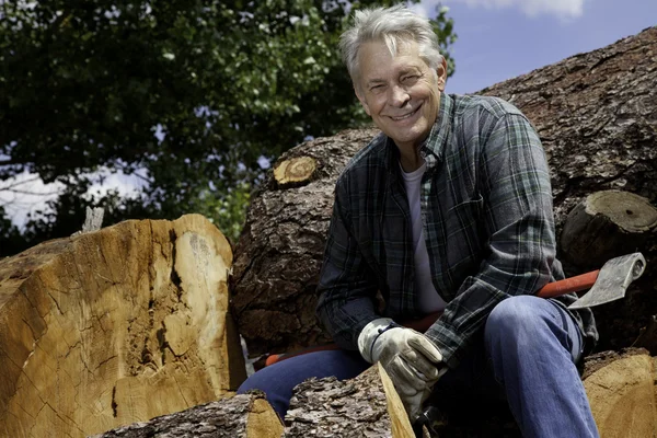 Hombre mayor sonriente sentado en troncos — Foto de Stock