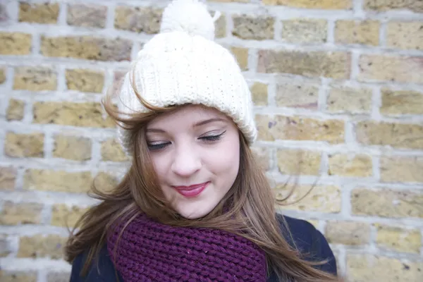 Happy young woman wearing knit hat and scarf looking down — Stock Photo, Image