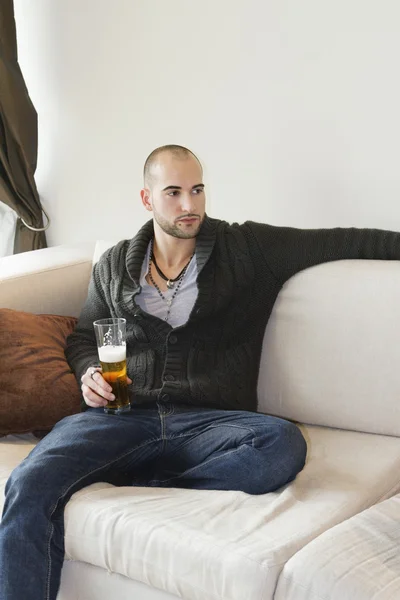 Jeune homme assis confortablement sur le canapé tenant une boisson — Photo