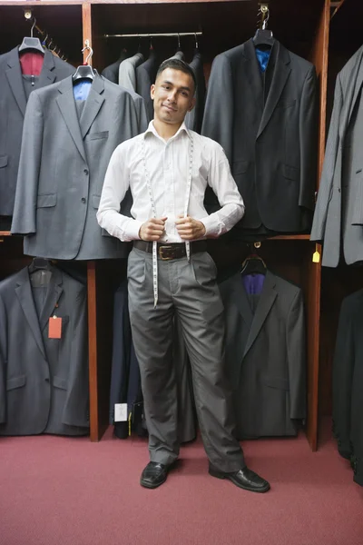 Portrait of young man posing with suits hanging in background